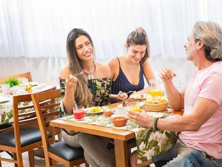 A dining area with wooden tables and chairs, a floral tablecloth, and a variety of breakfast foods and drinks.