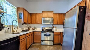 A kitchen with wooden cabinets, stainless steel appliances, and a window with curtains. - Modern Eco-Friendly Townhouse; Walk to Park & Recreation King Bed (Irving)