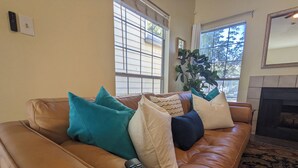 A brown leather sofa with teal and white cushions, a remote control, and a fireplace. - Modern Eco-Friendly Townhouse; Walk to Park & Recreation King Bed (Irving)