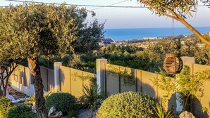 Ein Garten mit vielfältigen Pflanzen, einem Kiesweg und Blick auf das Meer.