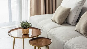 Ein modernes Wohnzimmer mit einer Couch, zwei runden Tischen, einer Pflanze und Blick durch große Fenster.