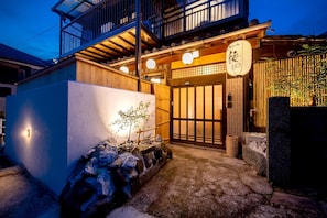 Um edifício japonês tradicional com fachada de madeira, entrada coberta por telhas e uma placa com caracteres japoneses.
