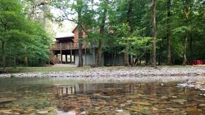 Eine Hütte mit einer Veranda mit Blick auf einen klaren Bach, umgeben von dichtem Wald.