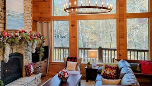 Ein gemütliches Blockhaus-Interieur mit Kamin aus Stein, Holzwänden, großen Fenstern und einer Ledersofa.