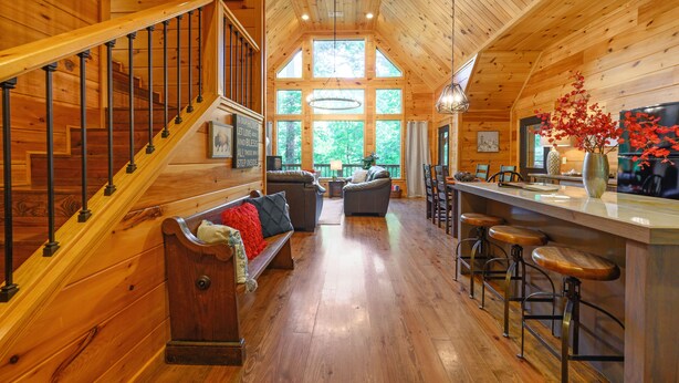 Ein geräumiges Holzhaus-Interieur mit Treppe, zwei Sofas, einem Essbereich und großen Fenstern.