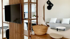 A modern living room with a wooden TV stand, a large mirror, a grey sofa, and a round coffee table. - Superior Suite with pivate jacuzzi (rethymno)
