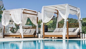 Two wooden beds with white canopies, a pool, and greenery in the background. - Superior Suite with pivate jacuzzi (rethymno)