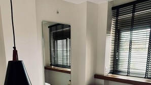 A hotel room with a bed, a round black chair, a hanging lamp, a round side table, and a window with blinds. - Superior Suite with pivate jacuzzi (rethymno)