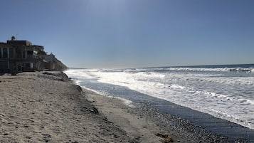 A beach with a building on the left, waves crashing onto the shore, and a clear sky.