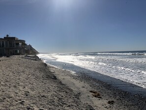 A beach with a building on the left, waves crashing onto the shore, and a clear sky.