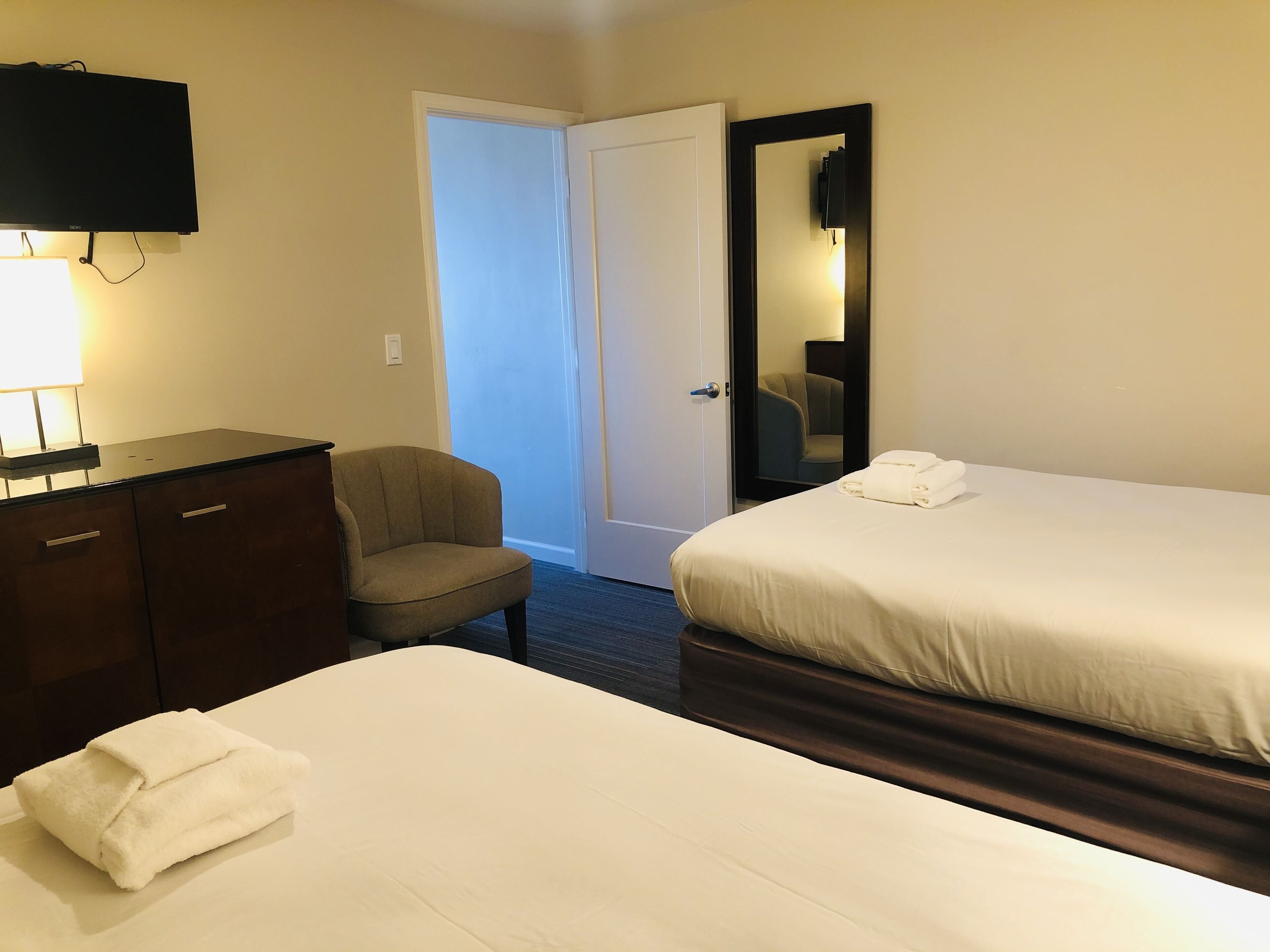 Ett hotellrum med två sängar, ett skrivbord, en stol, en TV och en dörr som leder ut till en korridor.