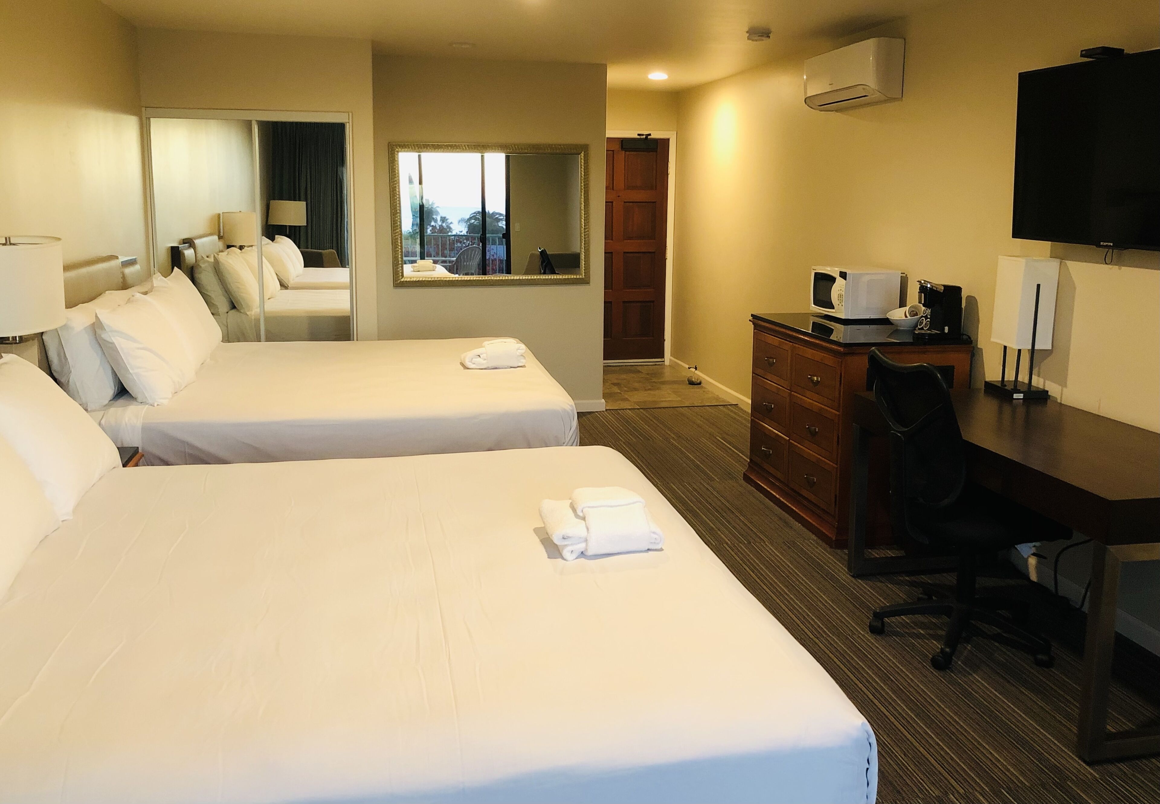 A hotel room with two beds, a desk with a computer, a TV, and a mirror.