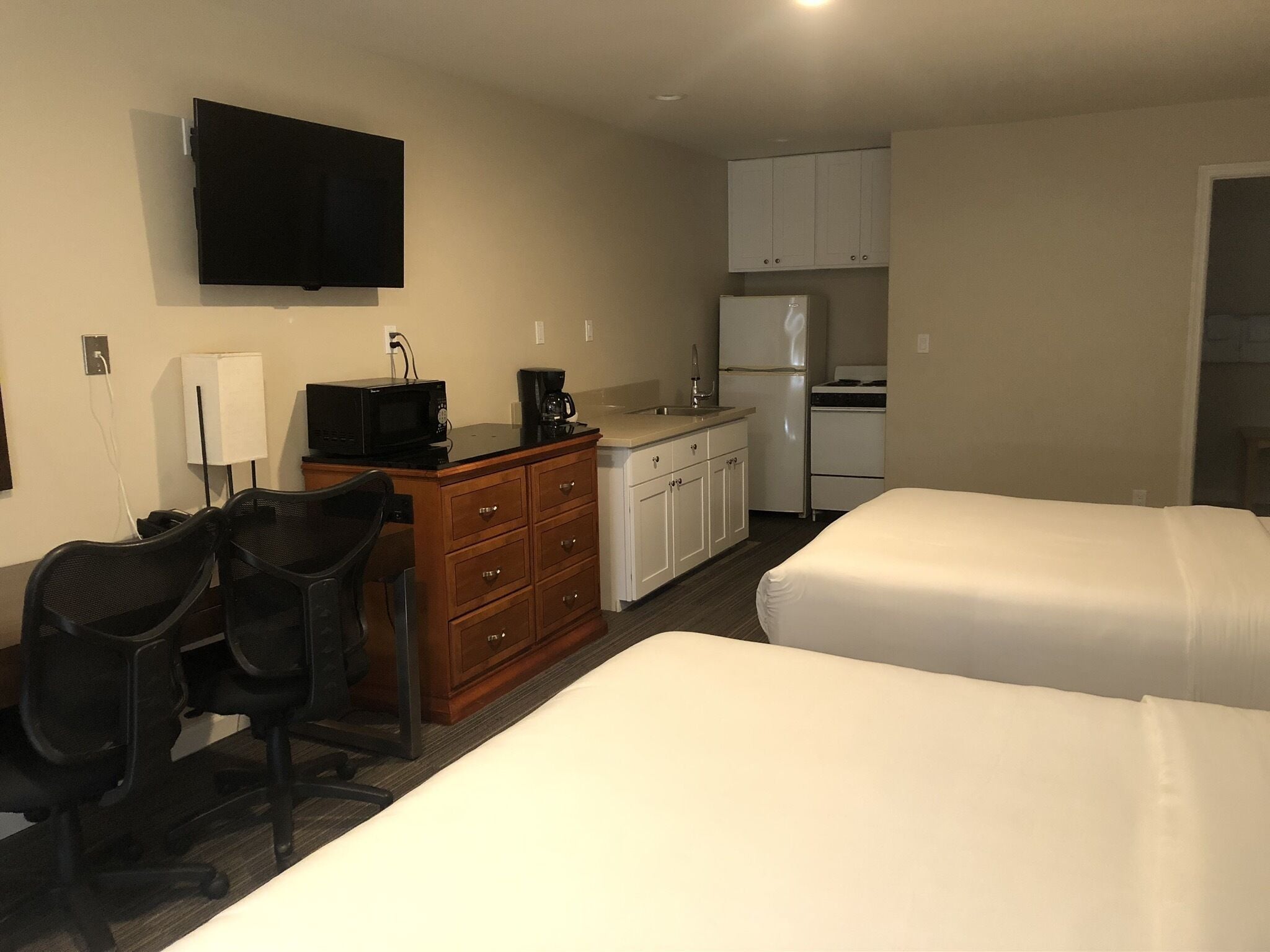Een hotelkamer met kitchenette, een aan de muur bevestigde televisie, een bureau met stoel en twee bedden.