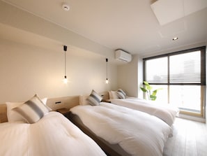 A hotel room with two beds, a window with blinds, an air conditioning unit, and a ceiling light fixture.