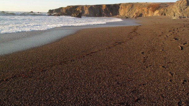 Ein Strand mit einer felsigen Klippe im Hintergrund.