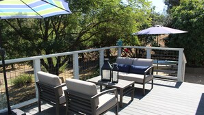 Eine Terrasse im Freien mit einer Couch, Stühlen und einem Tisch, umgeben von einem weißen Geländer und Bäumen.