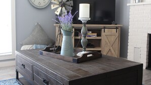 Ein Wohnzimmer mit Couchtisch aus Holz, einem Windrad, einer Kerze und einem Fernseher auf einem Schrank.