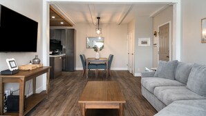 A modern living room with a wooden coffee table, grey sofa, and a dining area with a table and chairs.