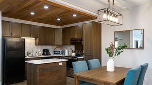 A modern kitchen with wooden cabinets, a central island, and a dining area with blue chairs.