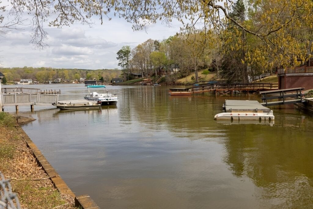 Une rivière paisible où des bateaux sont amarrés à un quai, le tout étant entouré d’arbres et bordé d’une promenade en bois.
