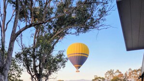 A hot air balloon in the sky, a grassy field, and a wooden deck with chairs. - iyla Estate - Your exclusive Vineyard & Cottage stay @ Pokolbin, Hunter Valley! (Pokolbin)