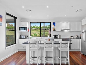 Een moderne keuken met witte kastjes, een groot eiland met barkrukken, een ingebouwde oven en uitzicht op een wijngaard door het raam.