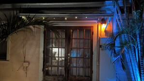Une entrée de maison avec une porte en bois, un petit porche et un réfrigérateur.