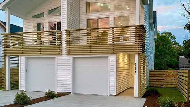 A modern two-story house with a covered front porch, a garage, and a small backyard with a wooden fence. - MODERN Beach Home! Dogs Welcome! 6 Passenger Golf Cart & Free Town of CB Parking (Carolina Beach)