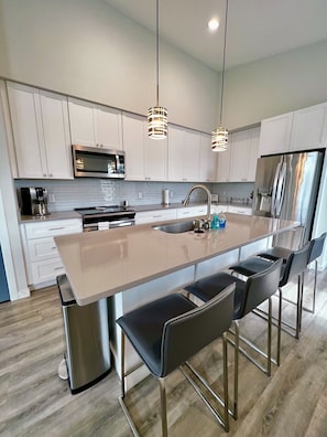 A modern kitchen with white cabinets, stainless steel appliances, a large island with bar stools, and pendant lighting.