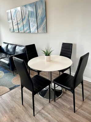 Un comedor con una mesa redonda, cuatro sillas negras, una planta en maceta y un sofá de cuero negro.