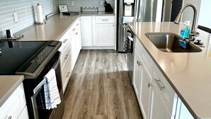 A modern kitchen with white cabinets, a stainless steel refrigerator, a built-in oven, and a sink with a faucet. - MODERN Beach Home! Dogs Welcome! 6 Passenger Golf Cart & Free Town of CB Parking (Carolina Beach)