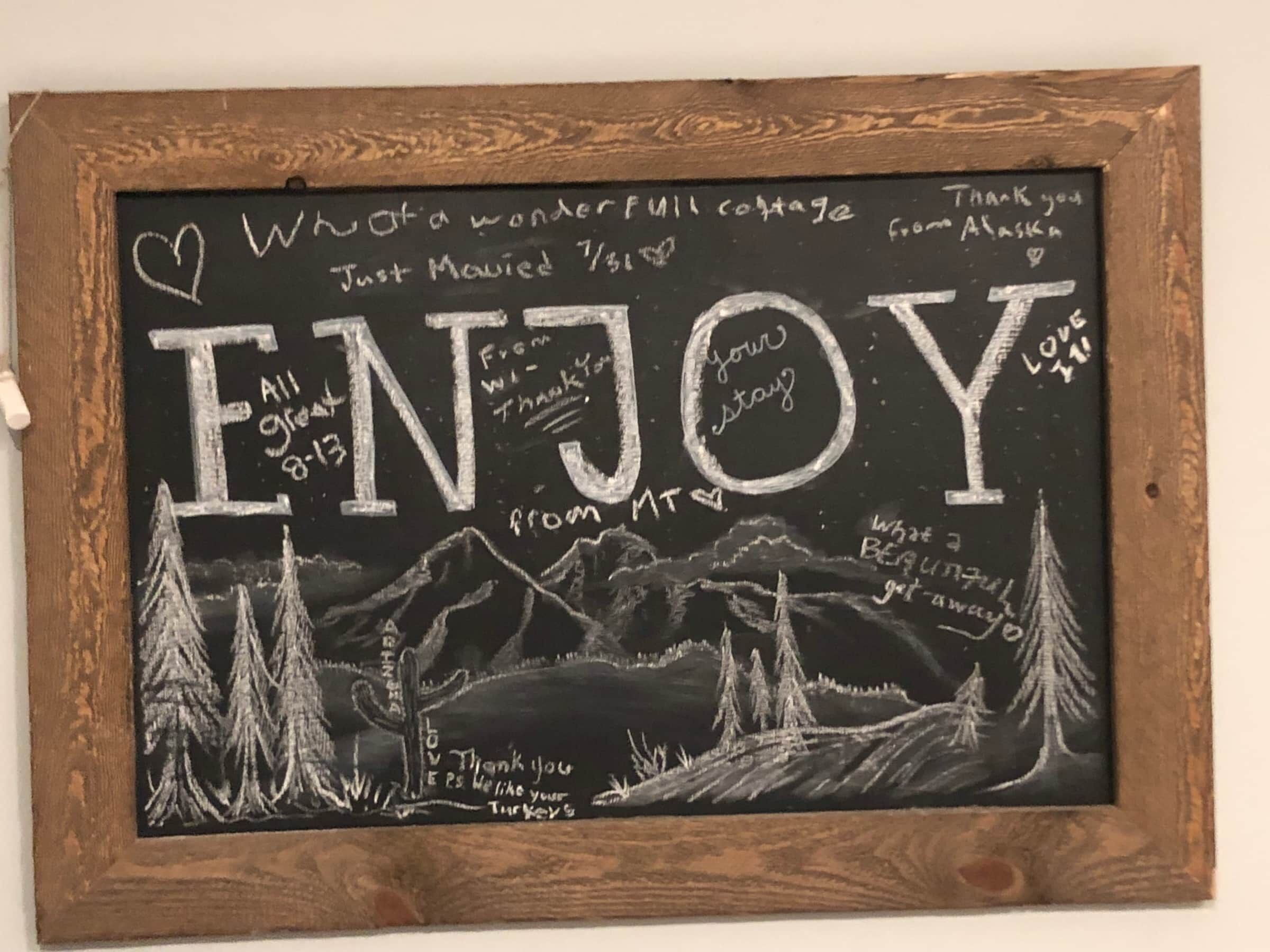 A chalkboard with 'ENJOY' written in large letters, surrounded by handwritten messages and a landscape drawing.