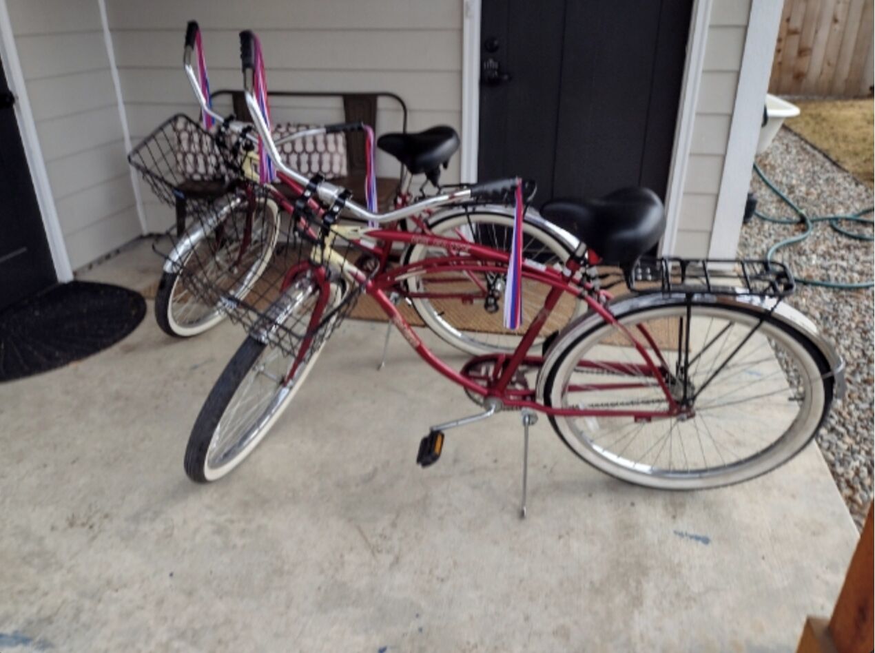 A red bicycle with a basket and a rear rack, parked on a concrete surface.