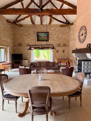 A rustic interior with a stone wall, wooden ceiling beams, a round dining table, and a fireplace. - Homerez - "Sigoulès villa with pool" (Sigoulès)