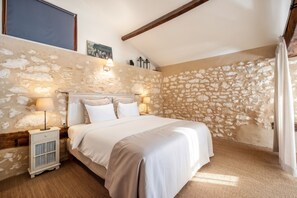 A bedroom with a stone wall, a bed with white linens, a nightstand, and a lamp. - Homerez - "Sigoulès villa with pool" (Sigoulès)
