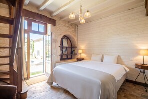 A bedroom with a bed, two bedside lamps, a wooden headboard, a stone wall, and a door leading outside.