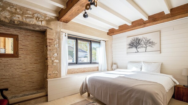 Un dormitorio con una cama grande, una ventana con cortinas, techo de madera y un cuadro en la pared.
