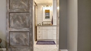 Un pasillo que conduce a un baño con armarios blancos, un espejo y una alfombra morada.