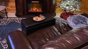 A cozy living room with a fireplace, leather sofa, and a Christmas tree.