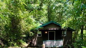A rustic cabin with a porch, surrounded by dense greenery.