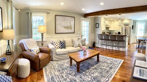A spacious living room with a brown leather armchair, a white sofa, and a wooden coffee table. A large map is displayed on the wall, and the room has hardwood flooring.