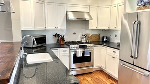 A modern kitchen with white cabinets, stainless steel appliances, a wooden countertop, and a black backsplash.