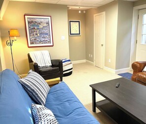 Una sala de estar con un sofá azul, un sillón negro, una mesita de centro y un mapa enmarcado en la pared.