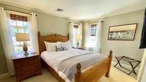 A neatly arranged bedroom with a wooden bed, two bedside tables with lamps, a wooden nightstand, and a framed picture on the wall.