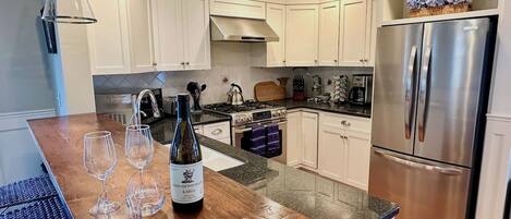 A modern kitchen with white cabinets, a stainless steel refrigerator, and a wooden island with wine glasses and a bottle.