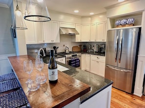A modern kitchen with white cabinets, a stainless steel refrigerator, and a wooden island with wine glasses and a bottle.