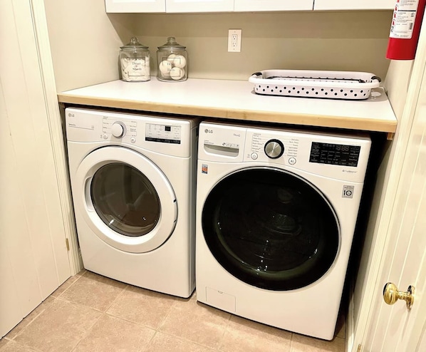 A laundry area with two white washing machines, a white countertop, and two glass jars on the shelf.