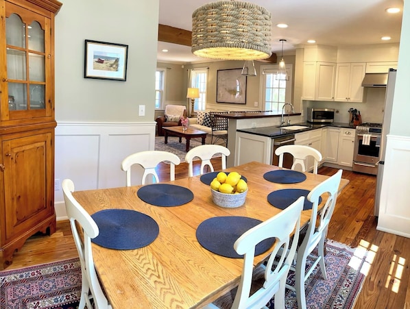 A dining area with a wooden table, white chairs, and a fruit bowl.