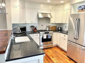 A modern kitchen with white cabinets, stainless steel appliances, a granite countertop, and a wooden floor.