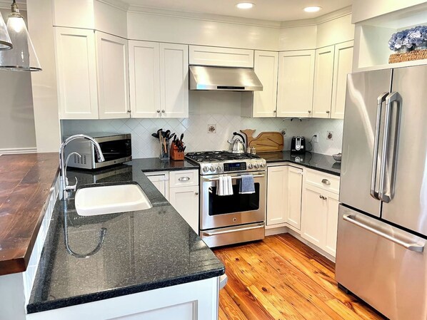 Una cocina moderna con armarios blancos, electrodomésticos de acero inoxidable, encimera de granito y suelo de madera.